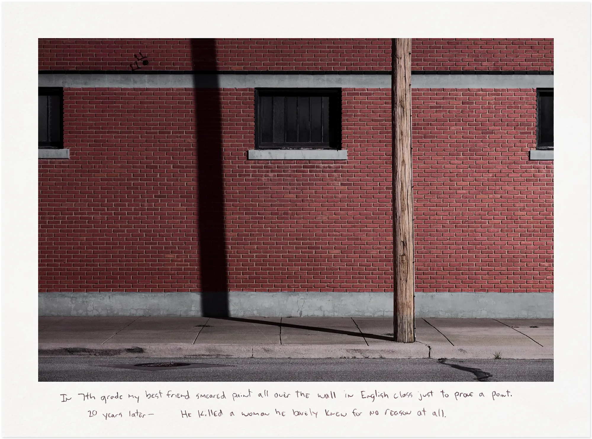 Wood telephone pole casting a shadow on a red brick wall at night.