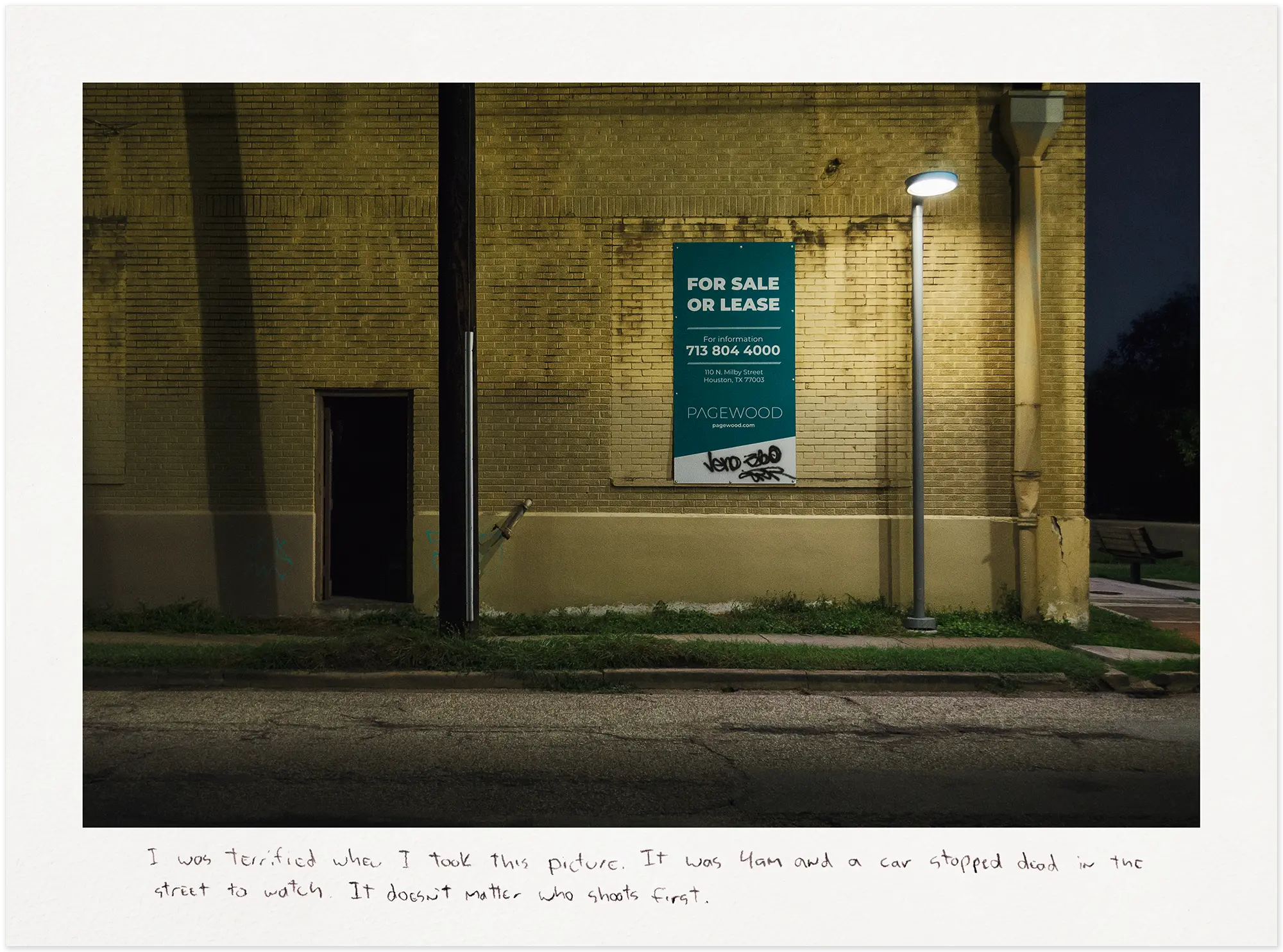 Yellow brick building with a green For Sale sign at night.