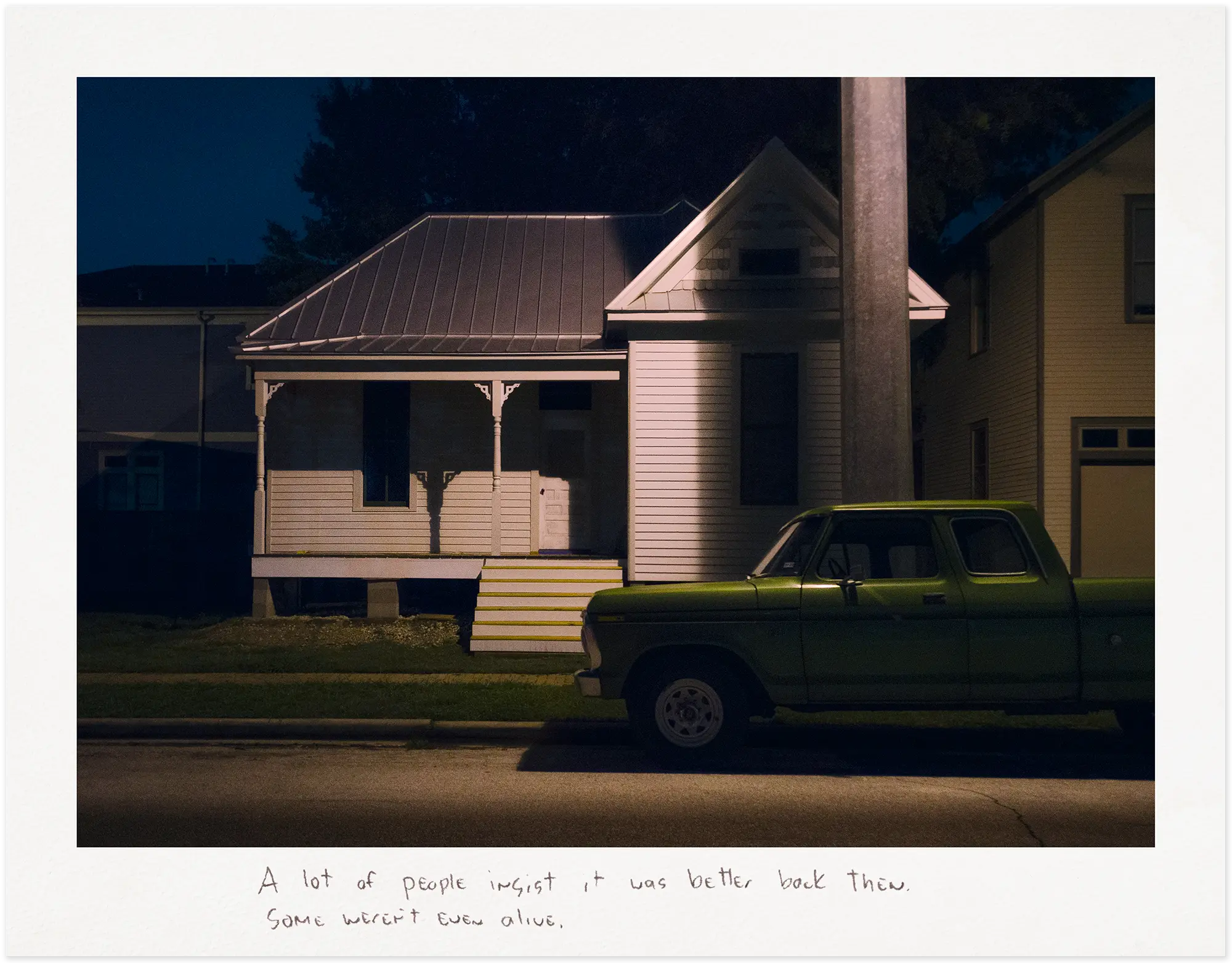 Green pick-up truck in front of a white house at night.
