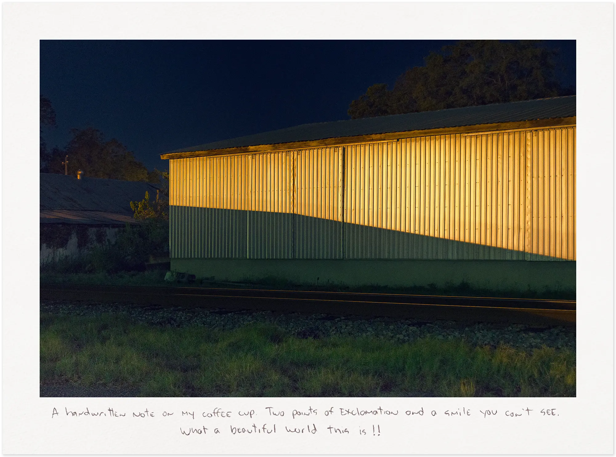 Metal barn near railroad tracks bathed in orange light at night.