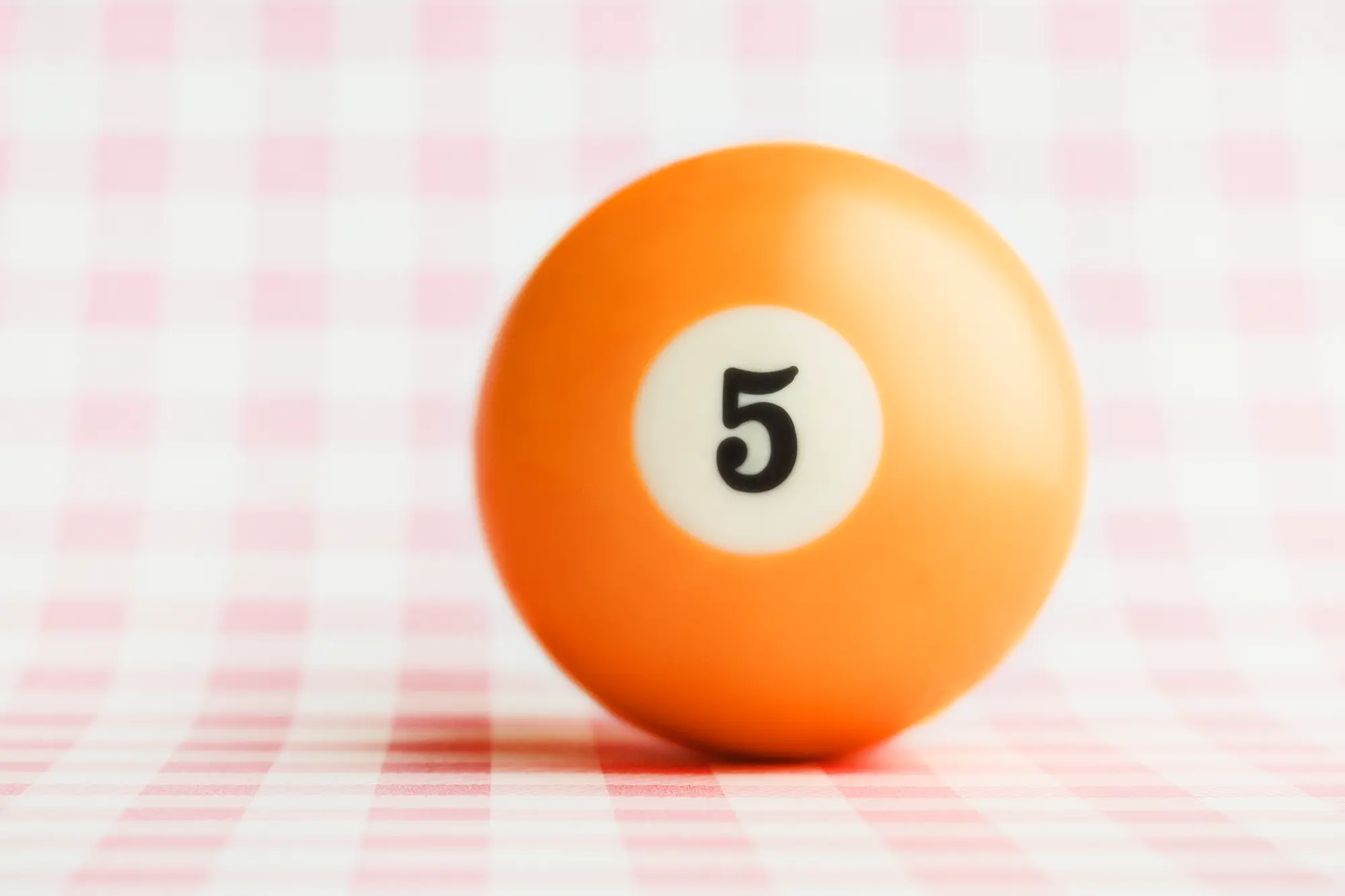 Solid orange billiard ball on a pink and white checkerboard background.