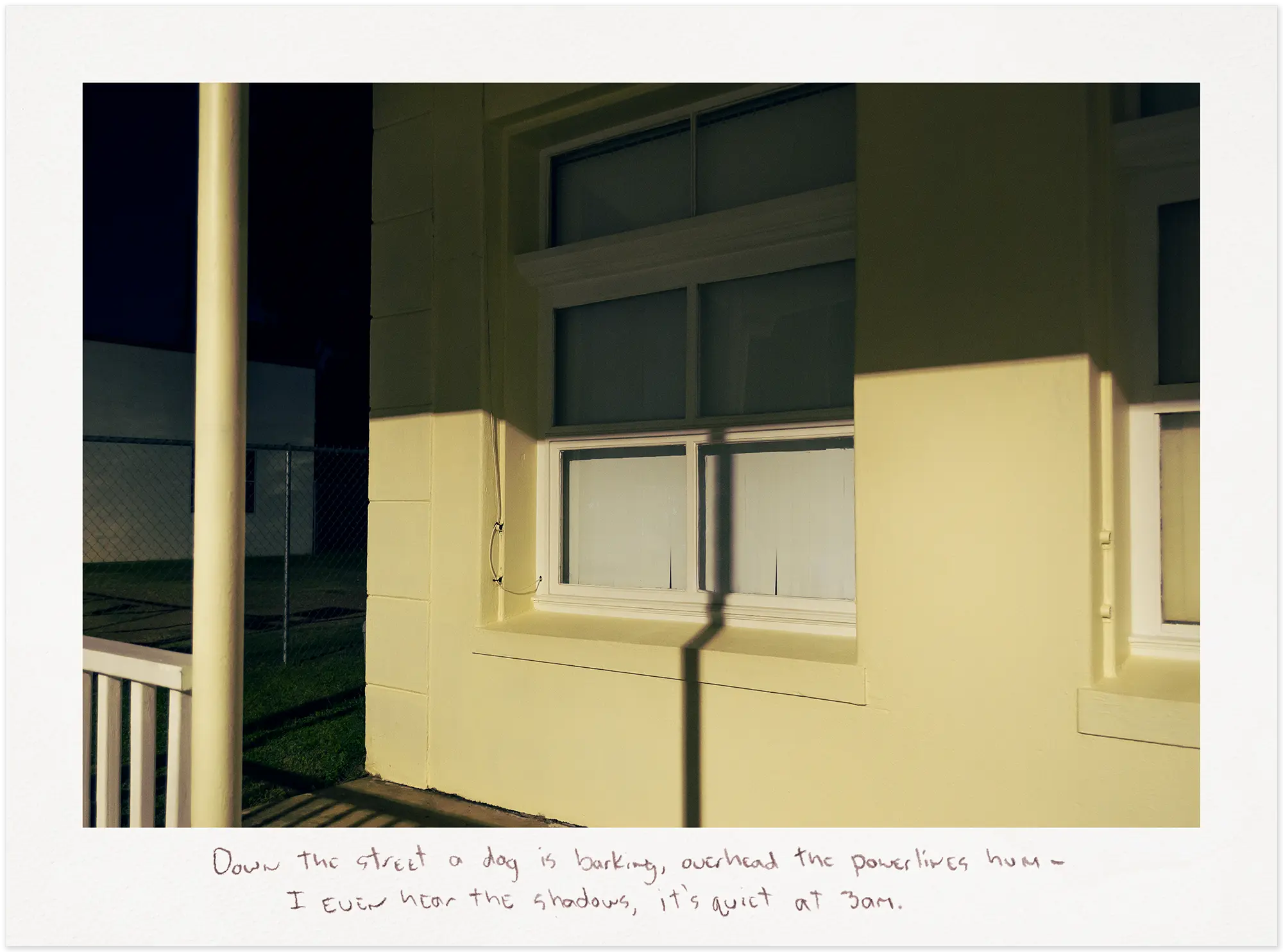 Shadow across the window of a yellow building at night.