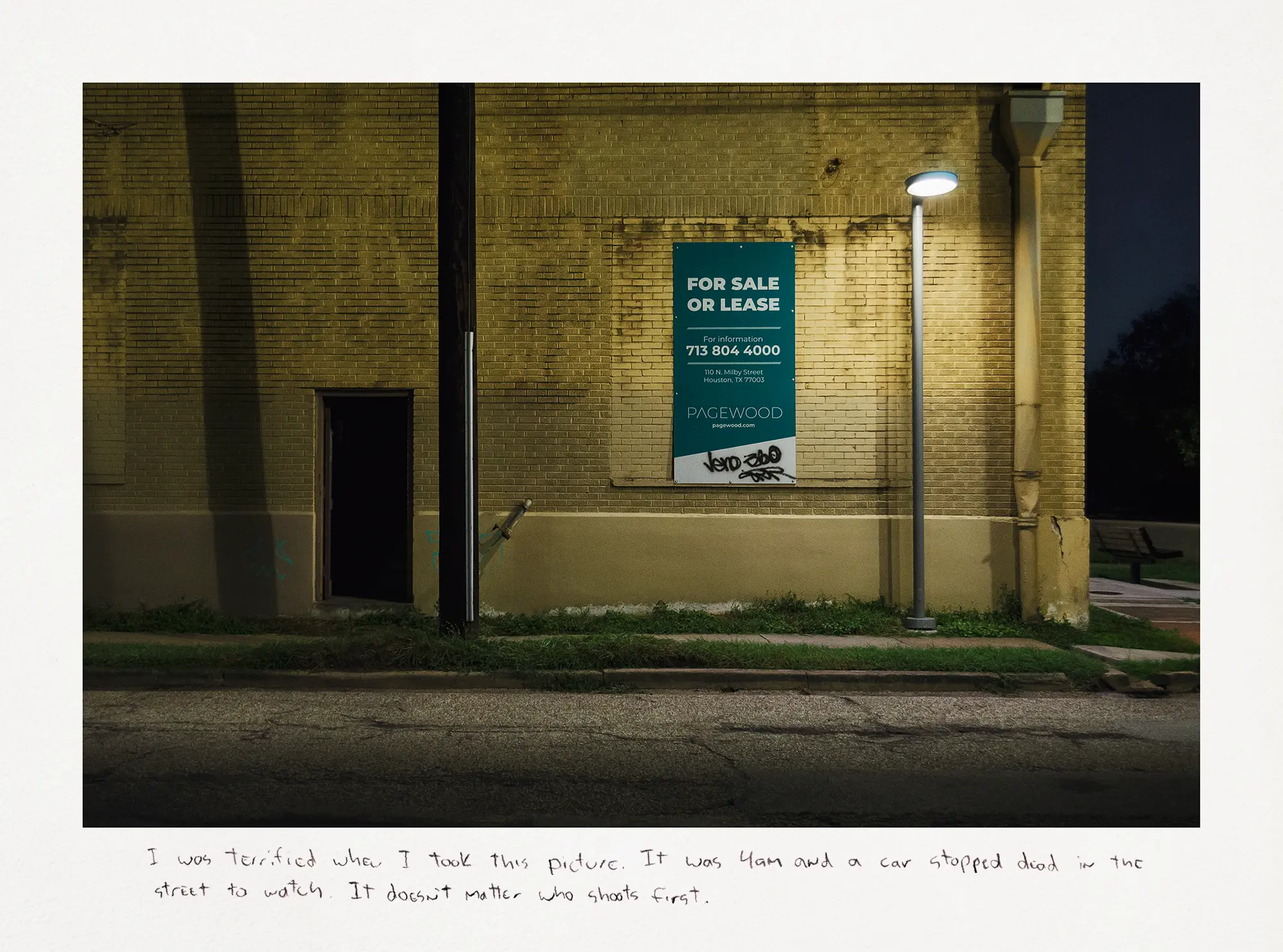 Nighttime photograph of a street lamp outside a yellow brick building with a green "For sale or lease" sign.