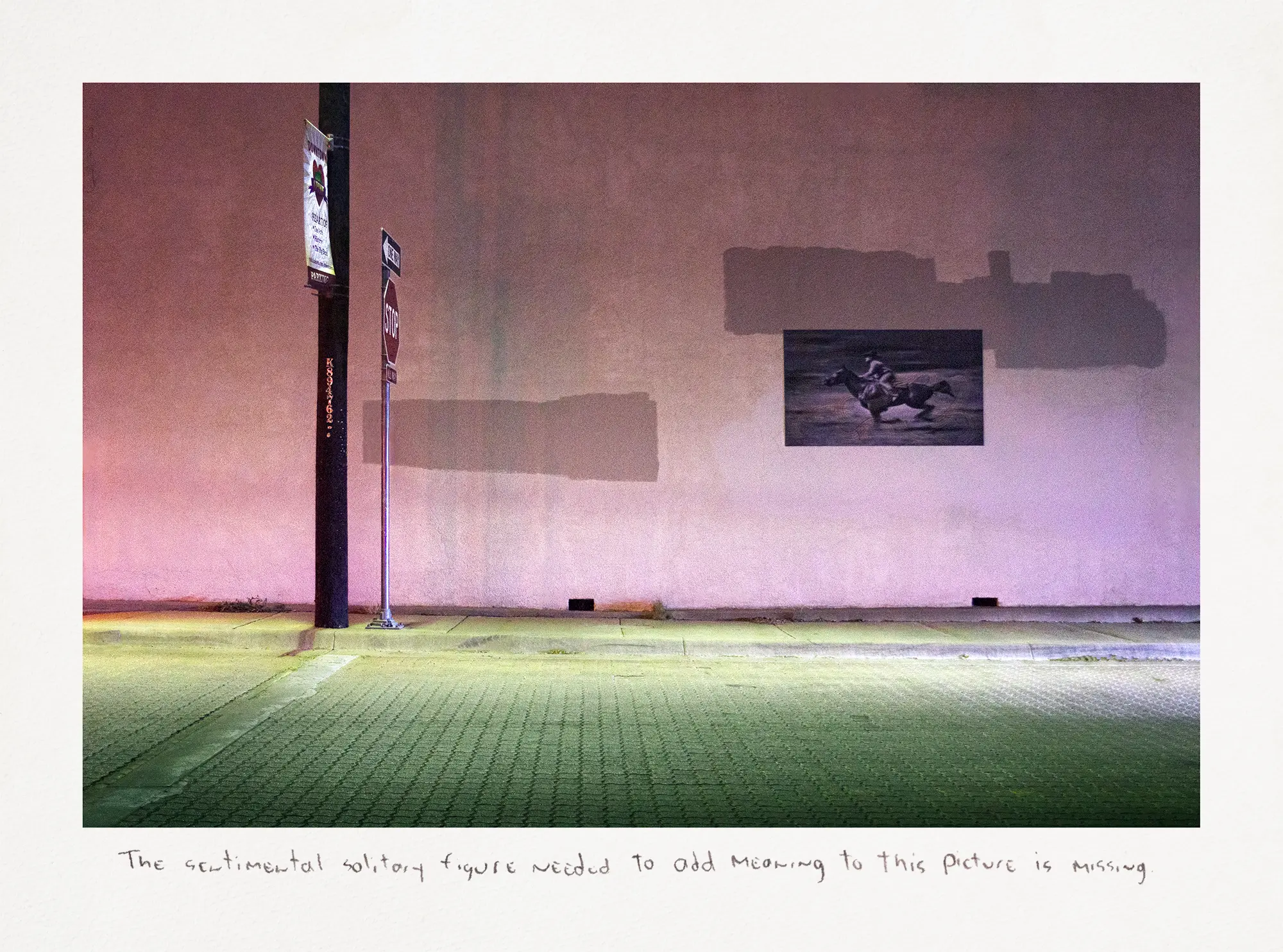 Photograph of a building featuring a pink exterior that showcases a small black-and-white image of a cowboy on horseback positioned. The scene is set alongside a street illuminated by green lighting.