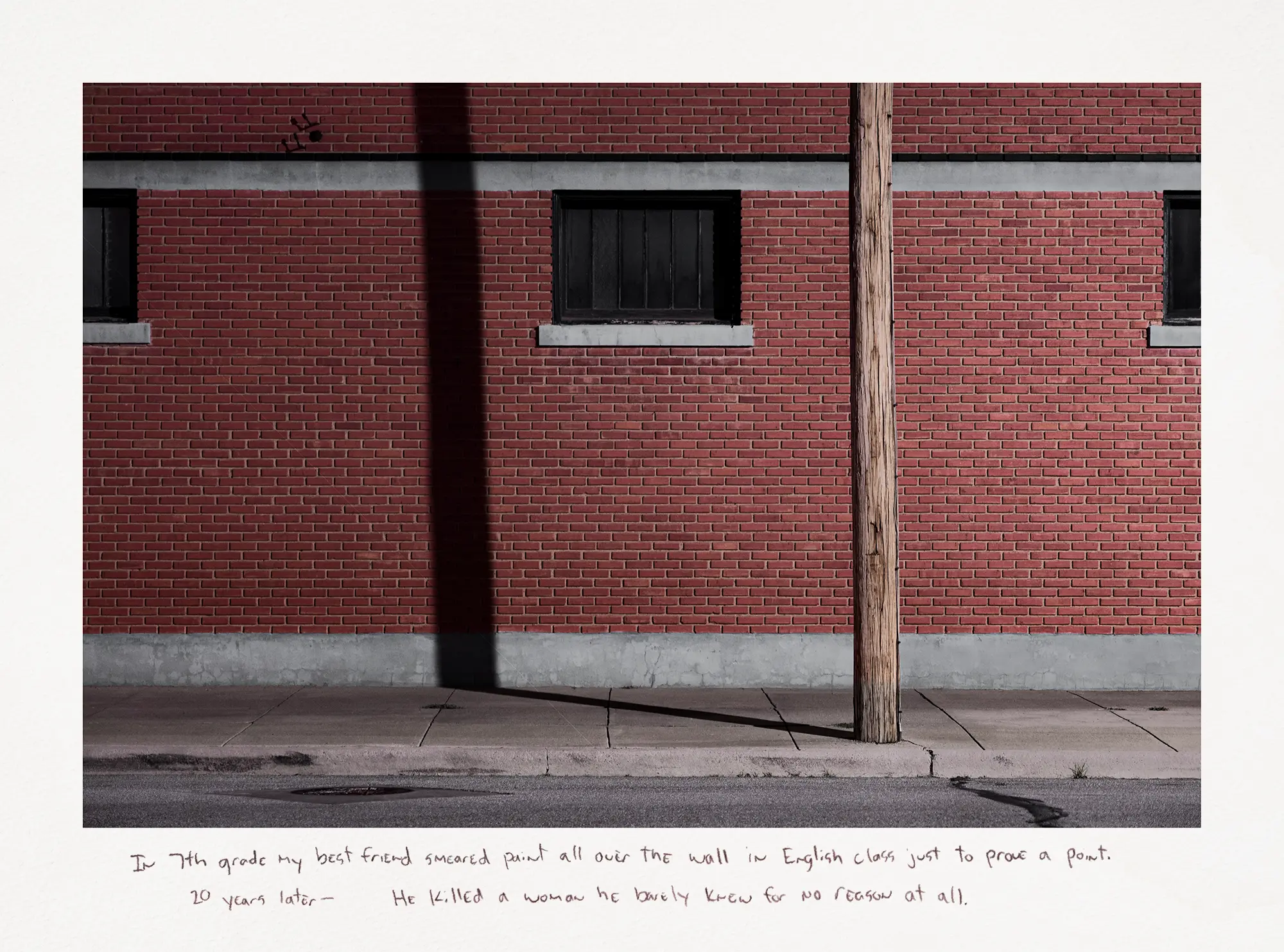 A photograph taken at night capturing a wooden telephone pole with its shadow cast against a red brick building.