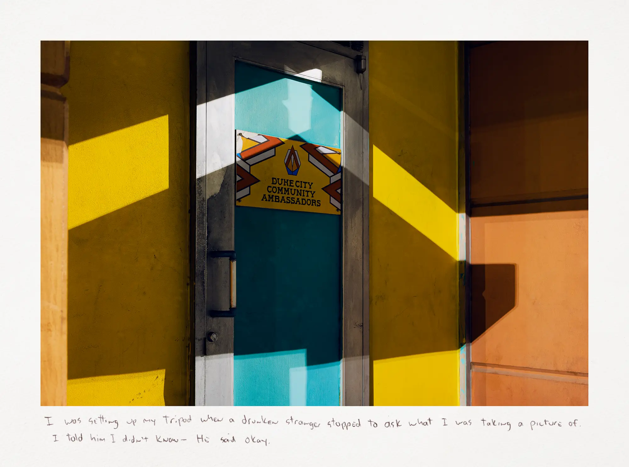 A nighttime color photograph of the blue, orange, and yellow door at the Duke City Community Ambassadors office.