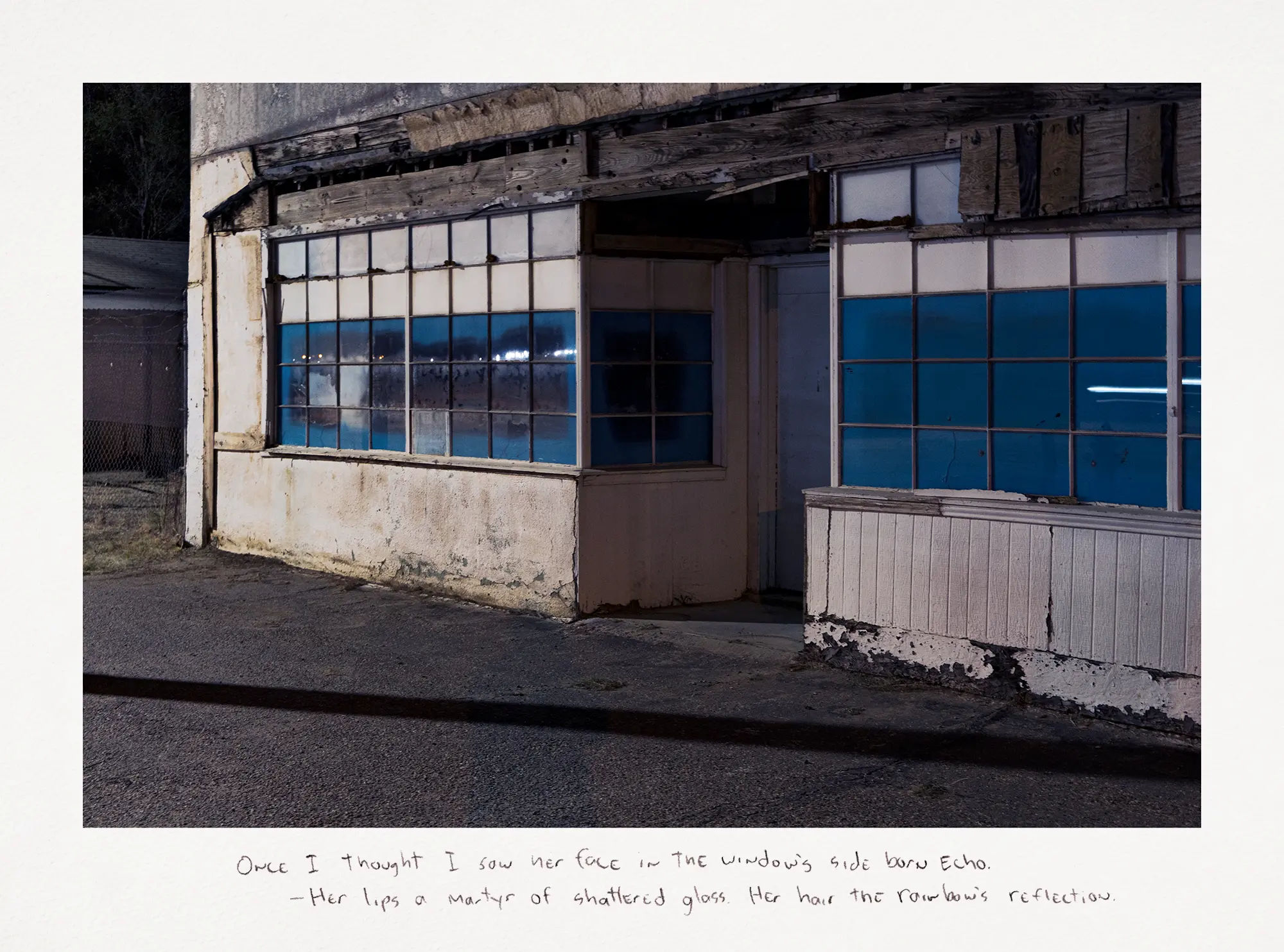 Night photograph of an abandoned building with blue-tinted windows and weathered white walls.